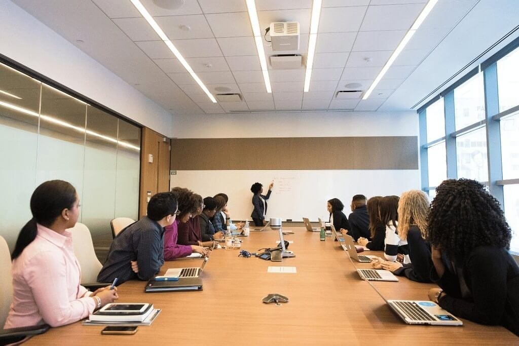 Office meeting with employees sitting around a table, focusing on a presentation.