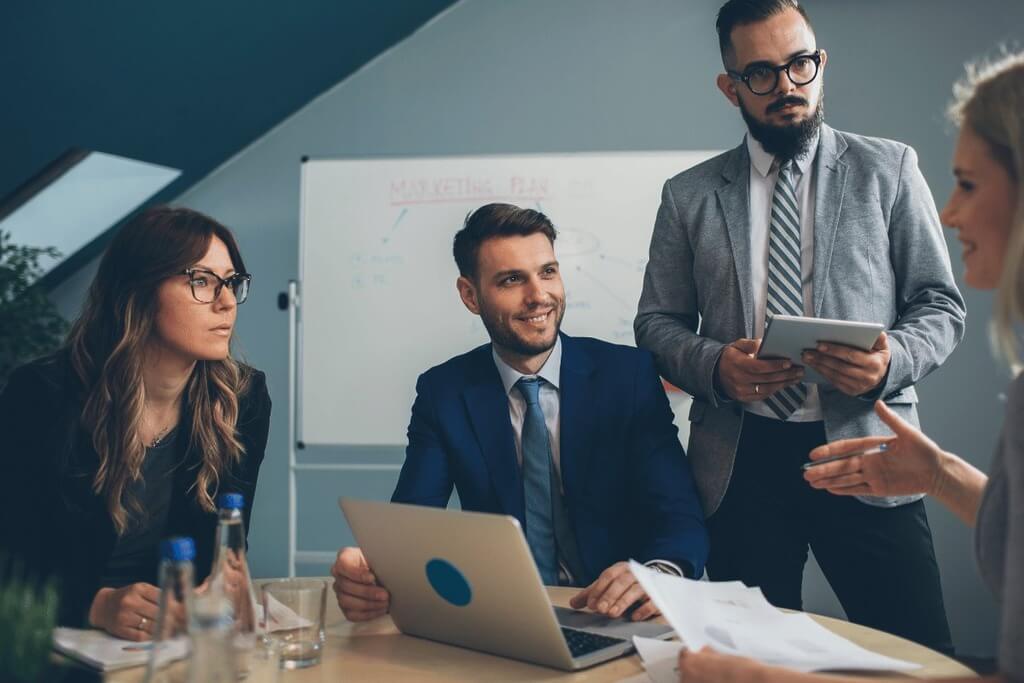 Business professionals discussing over documents with a whiteboard in the background.