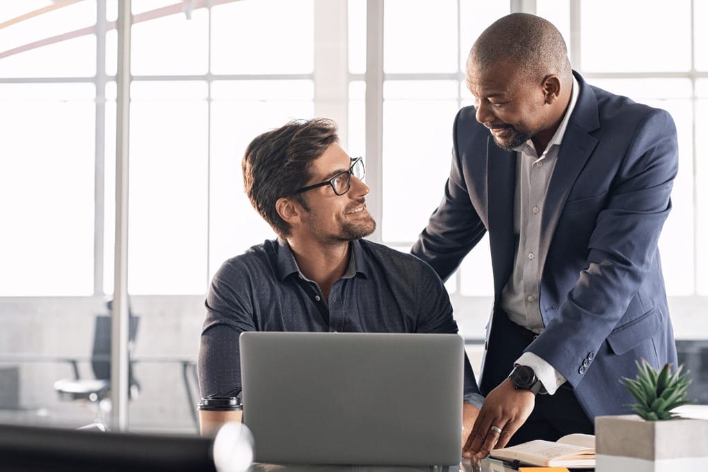 Two professionally dressed men are focused on a laptop, collaborating on a task or project.