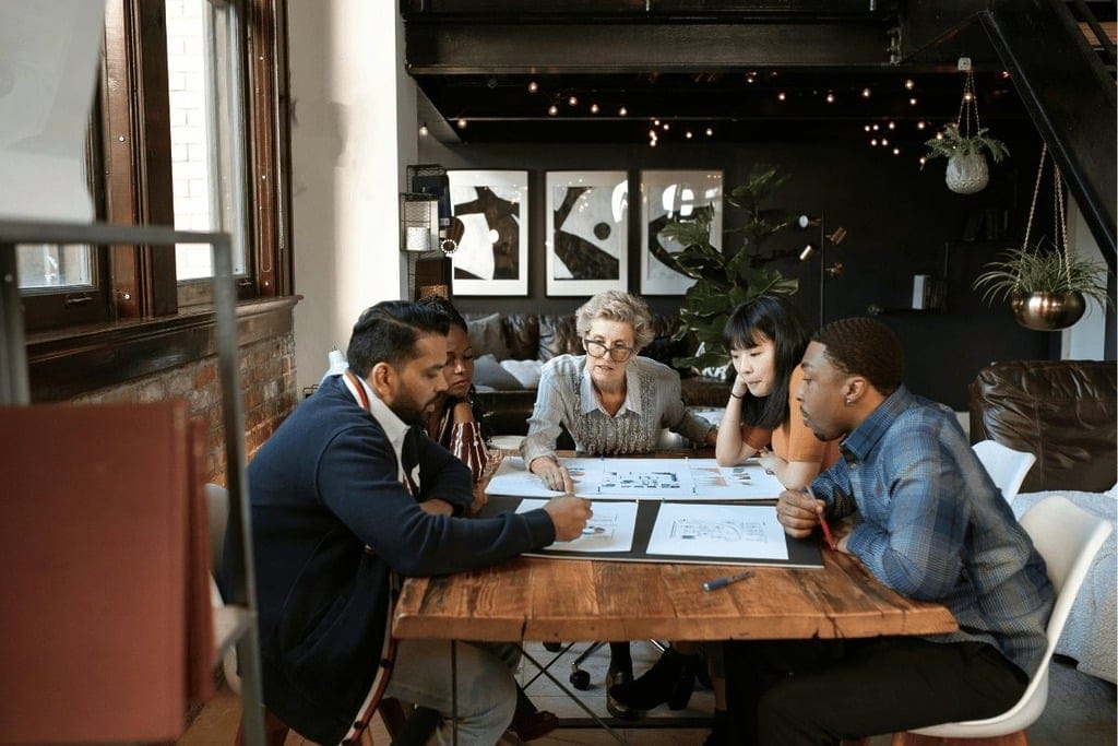 Group of colleagues discussing project plans and designs in a stylish, industrial-themed workspace.