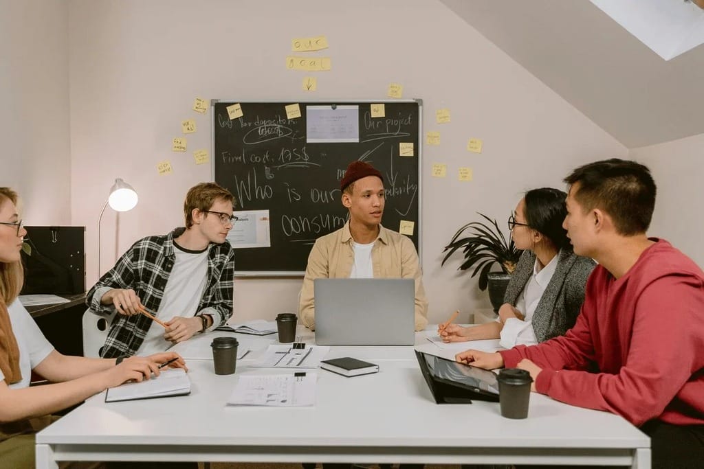 Team of five young professionals having a strategy meeting with a laptop and notes.
