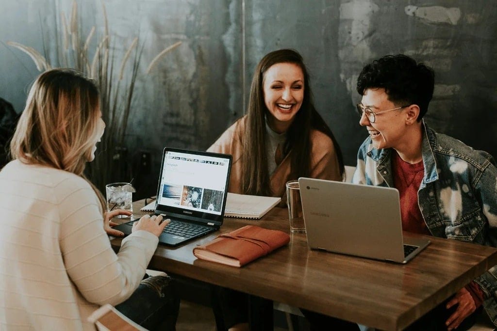 Happy friends using laptops and taking notes at a wooden table.