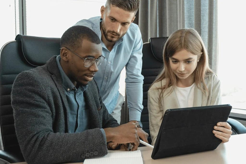 Three coworkers collaborating around a tablet during a meeting in a modern office.