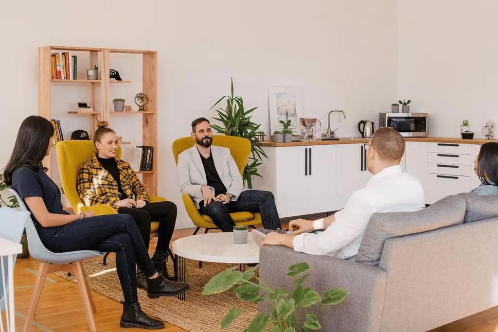 Office team holding a meeting in a stylish lounge area with plants and cozy furniture.