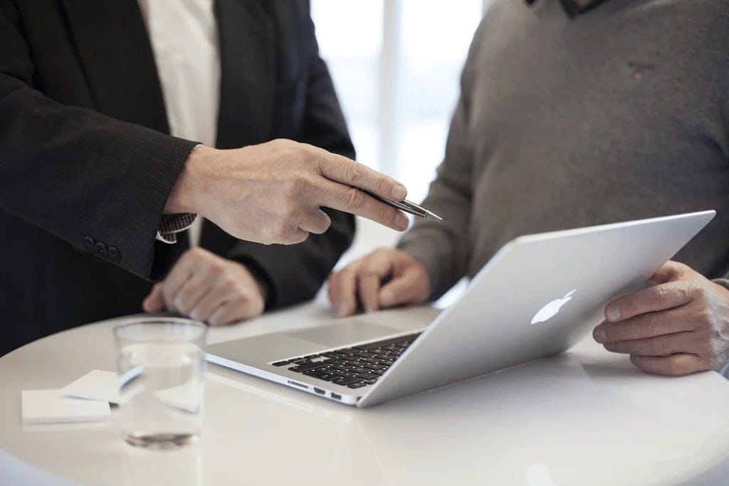 Two colleagues discussing work on a laptop in a modern office.