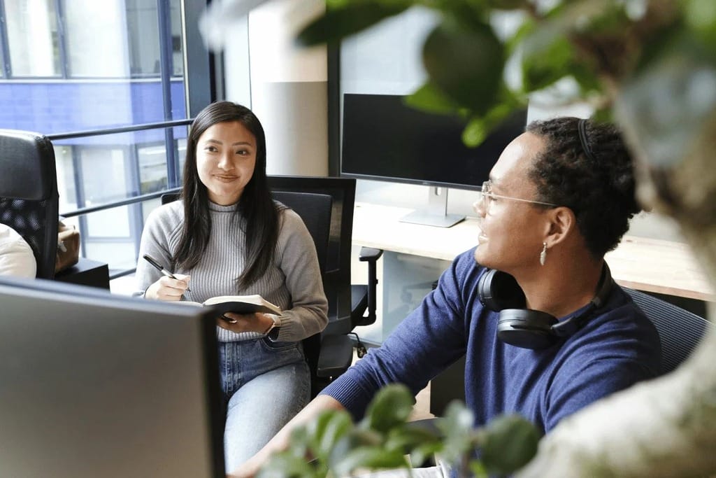 Smiling coworkers discussing work in a brightly lit, contemporary office.