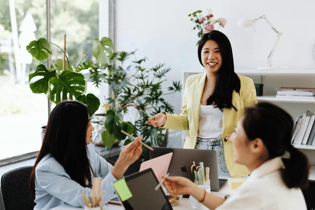 Three women collaborating in a bright office filled with plants.