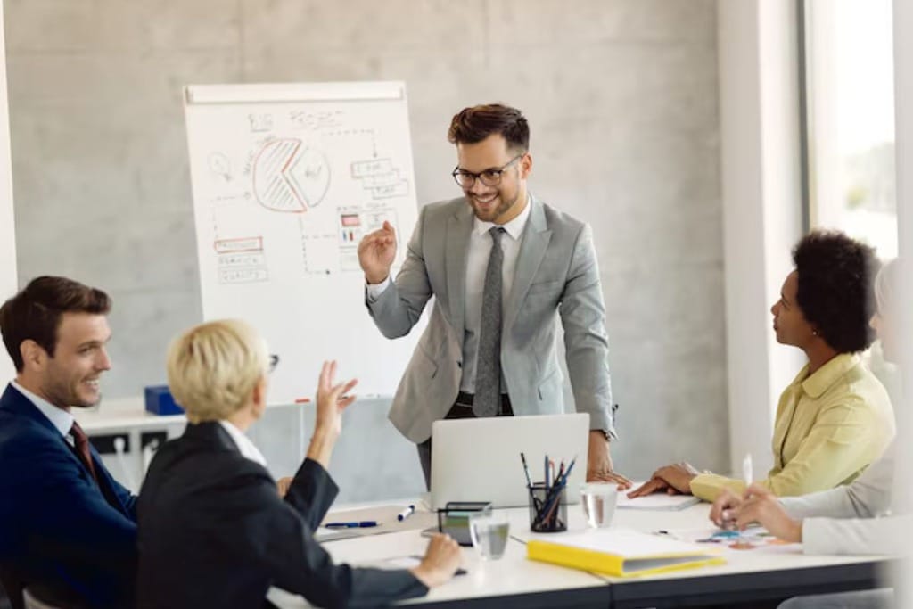 Four business professionals collaborating on a project, one standing and the others seating, in a bright modern office.