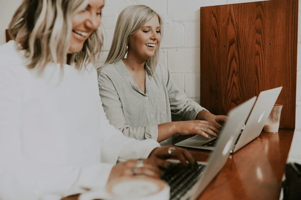 Happy women collaborating on their laptops in a shared workspace.