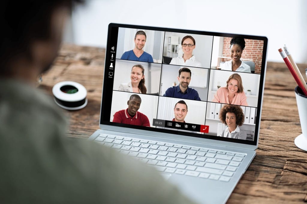 A person participates in a video conference on a laptop placed on a wooden desk.