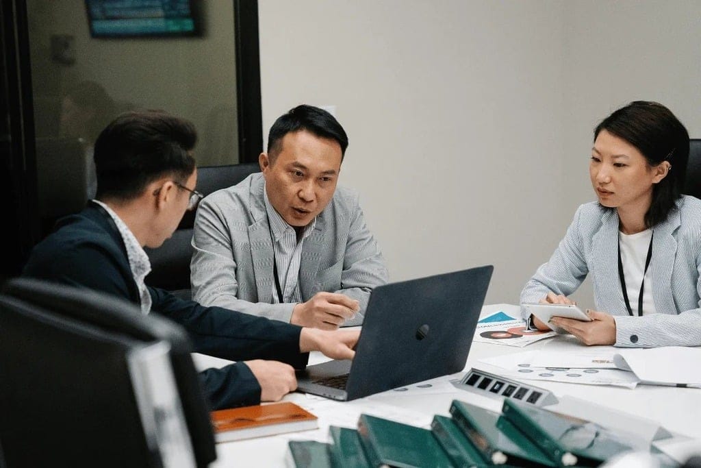 Three professionals collaborating around a table with laptops and documents.