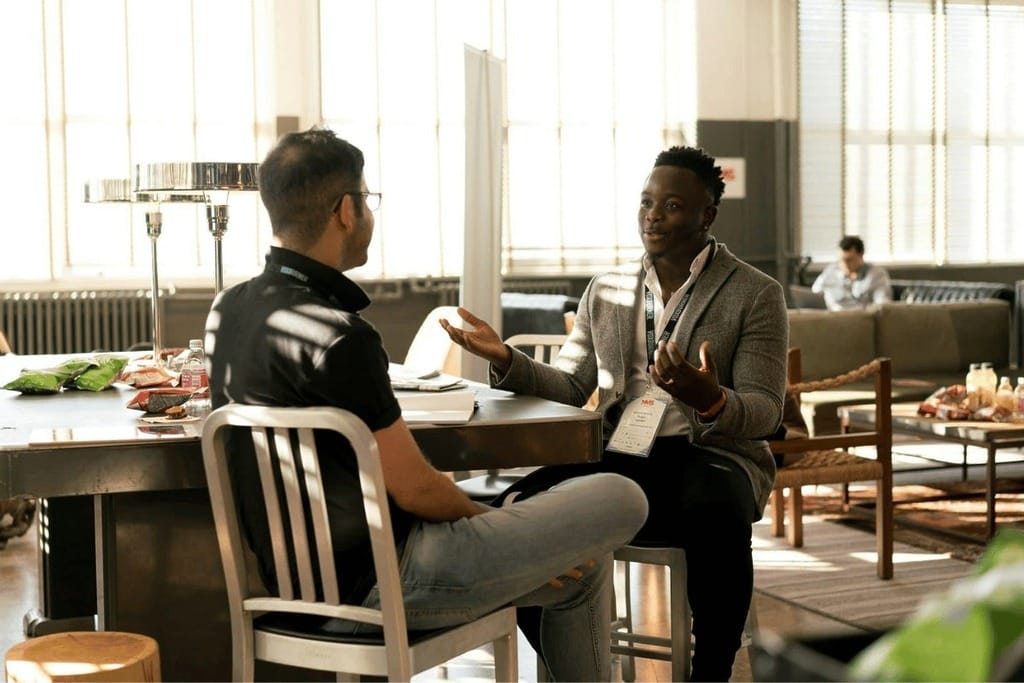 Professionals networking at a conference, seated at a high-top table with badges.