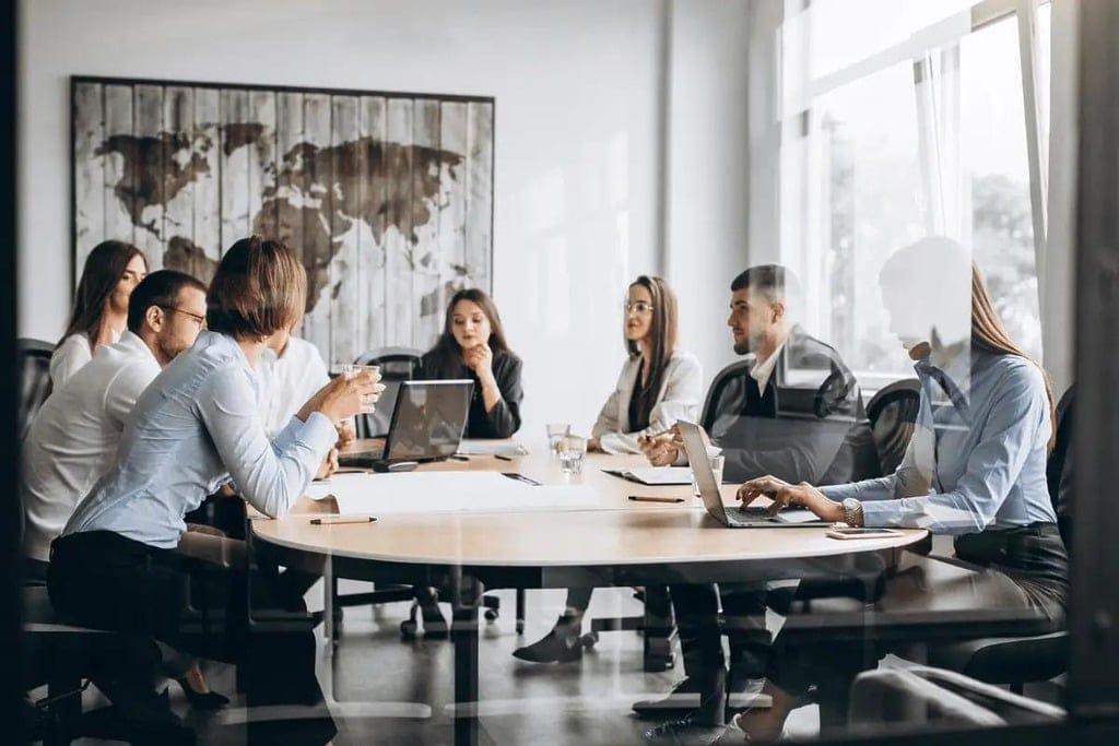 Colleagues engaged in a serious discussion during a team meeting, with laptops and documents spread across the table.