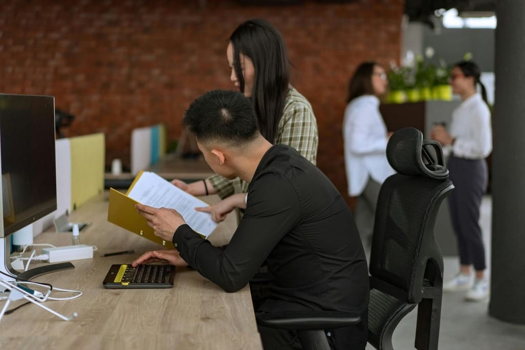 Office workers at desks with computers, one person reading a document.