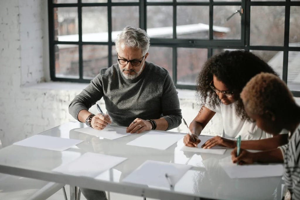 Team members in a bright room, and busy writing on a paper.