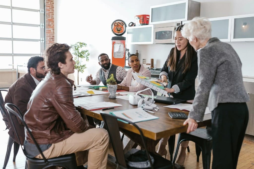 Group of people engaged in a meeting around a table with documents and a laptop.