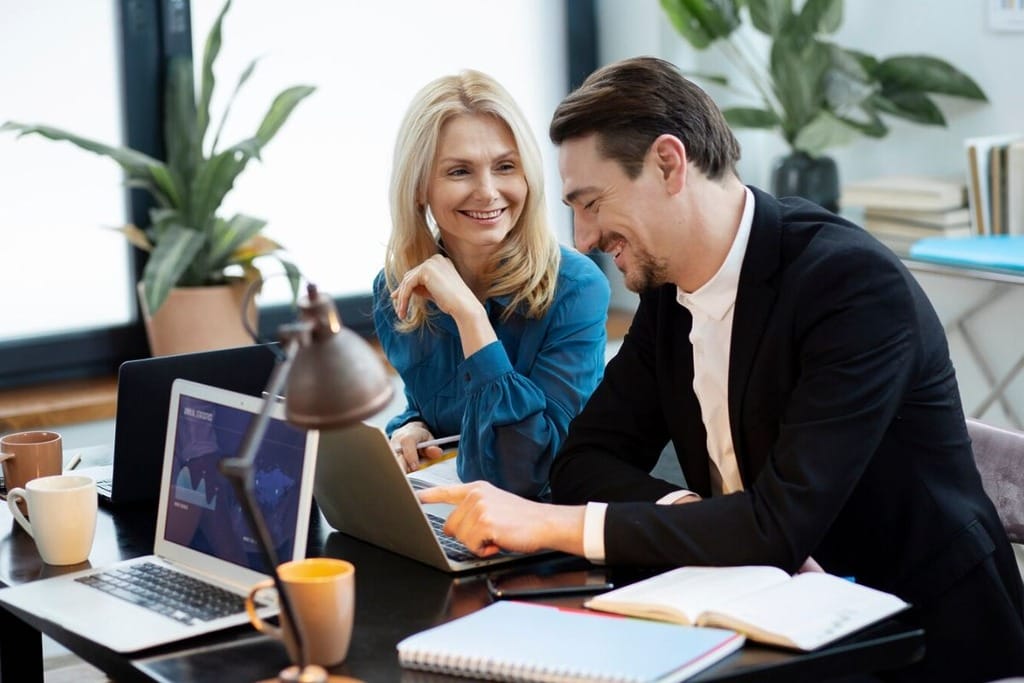 Two professionals reviewing documents and data on a laptop.
