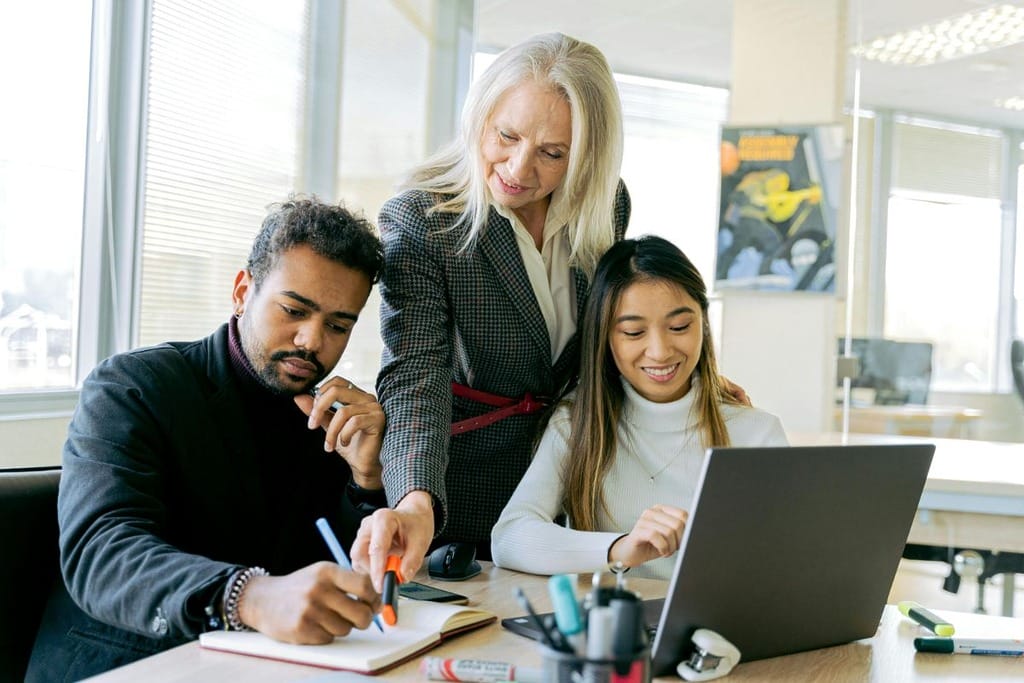 Three professionals collaborating around a laptop in a bright office setting.