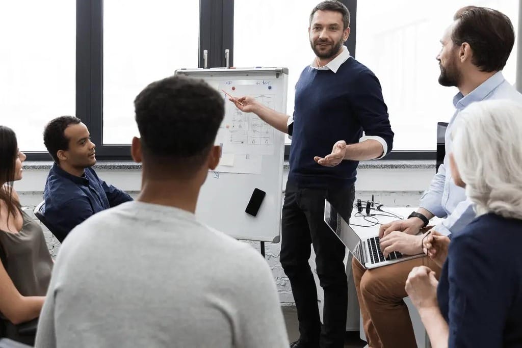 A business professional leading a presentation for a small group, using a whiteboard with diagrams and notes.