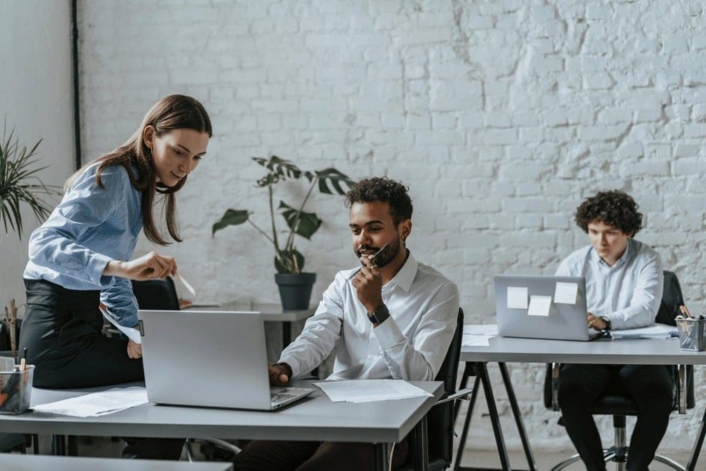 Three professionals working at laptops in a modern office setting.