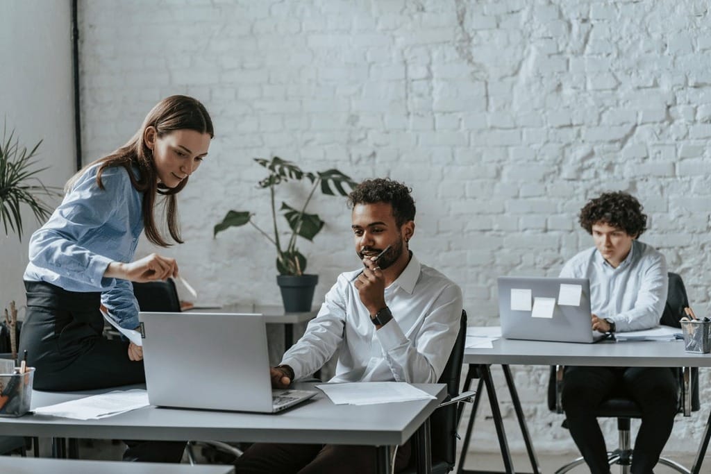 Three professionals working at laptops in a modern office setting.