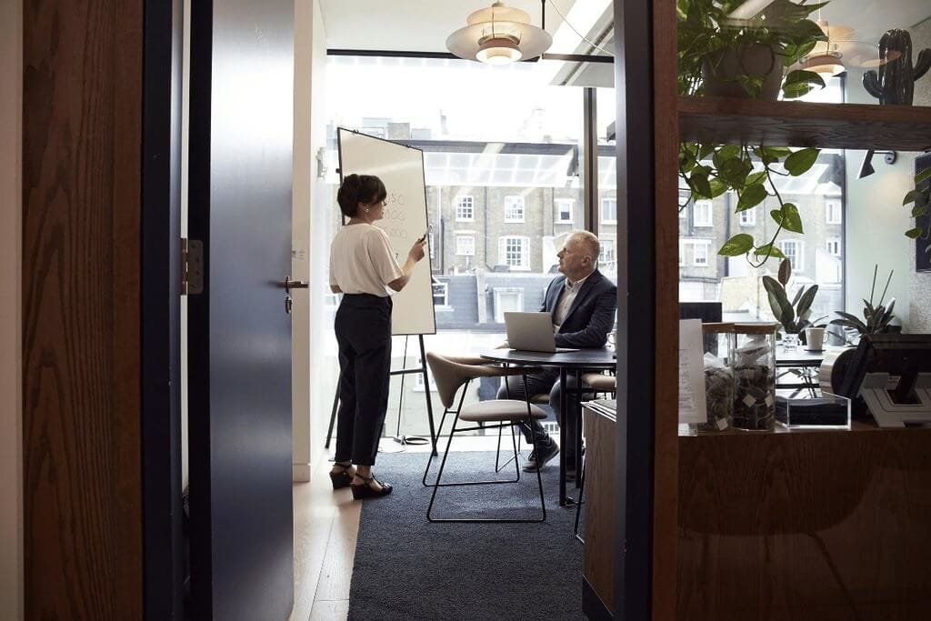 Woman giving a presentation on a whiteboard while a colleague listens attentively.