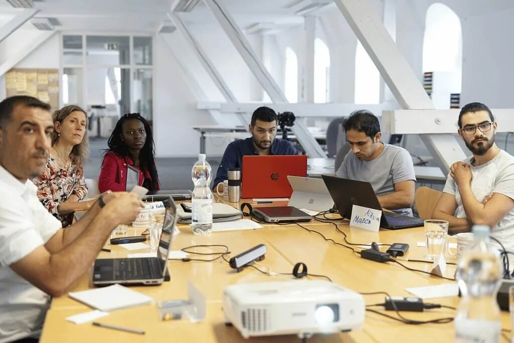 Group of professionals in a meeting with laptops and a projector on the table.