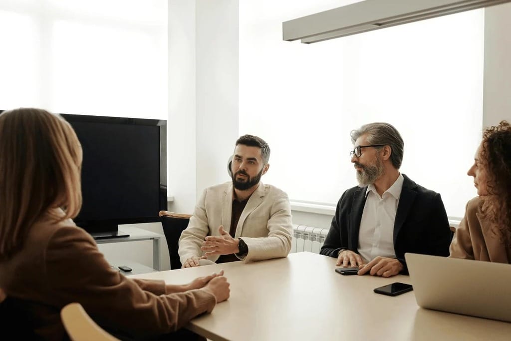 Four individuals engaged in discussion while seated at a table in a professional office environment.
