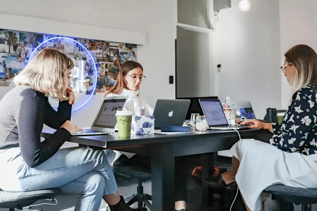 Female professionals collaborating in an office with laptops.