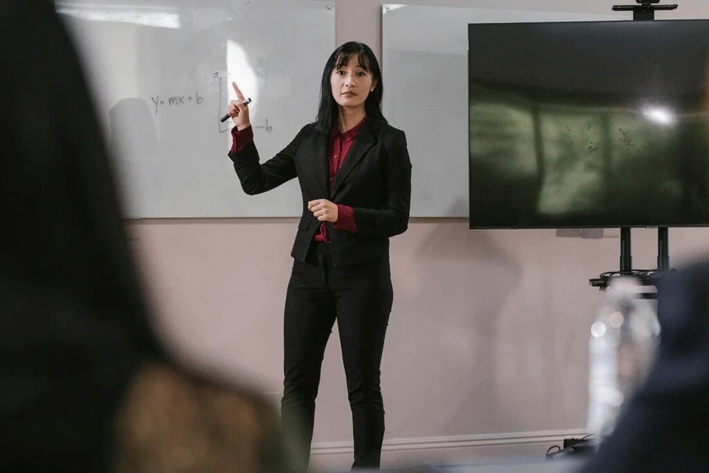 Person gesturing towards a whiteboard with mathematical equations in a presentation room.