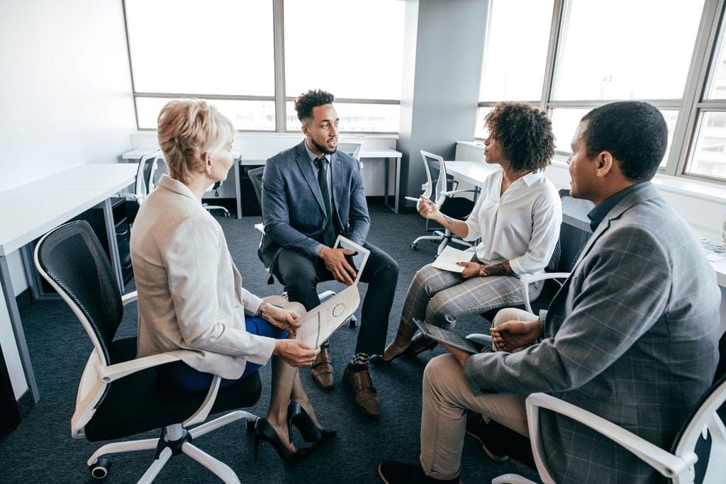 Woman in a white shirt leading a discussion with team members in a conference room.