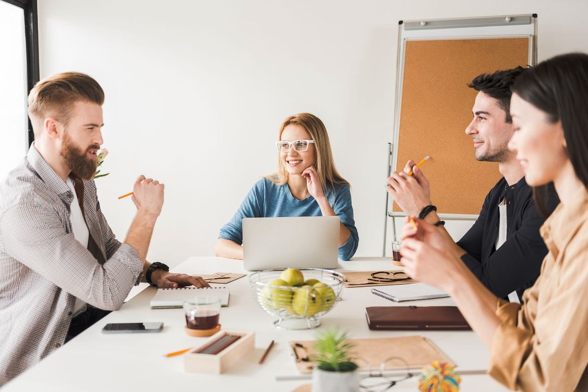 Four professionals in a meeting with laptops and notepads on a white table.
