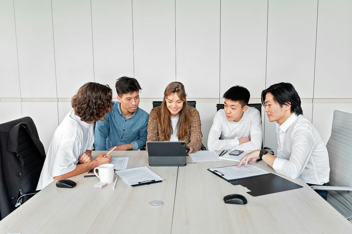 A group of five professionals sitting around a conference table with laptops and documents.