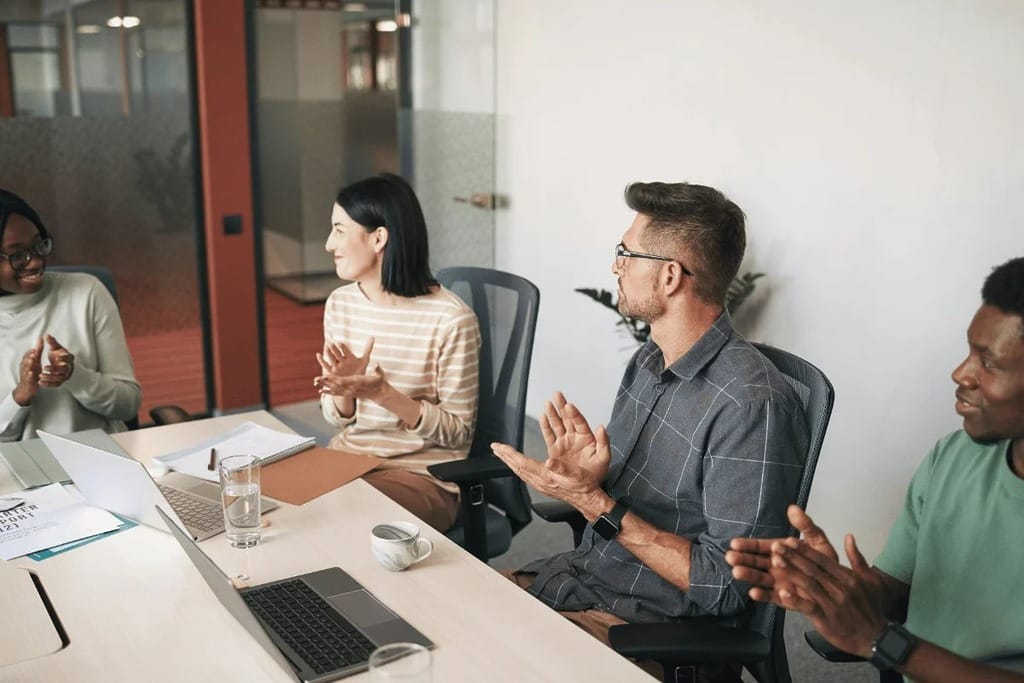 Colleagues clapping during a meeting in a modern office.