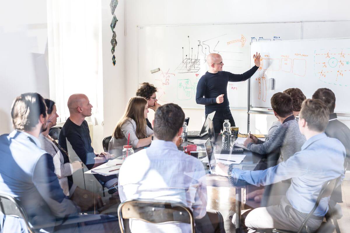 A person presenting at a whiteboard during a meeting with attentive colleagues.